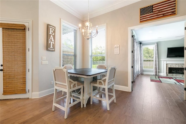 dining space featuring ornamental molding, wood-type flooring, a notable chandelier, and a brick fireplace