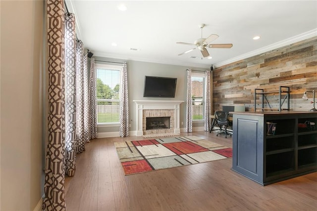 unfurnished living room with wood-type flooring, ornamental molding, ceiling fan, and a brick fireplace