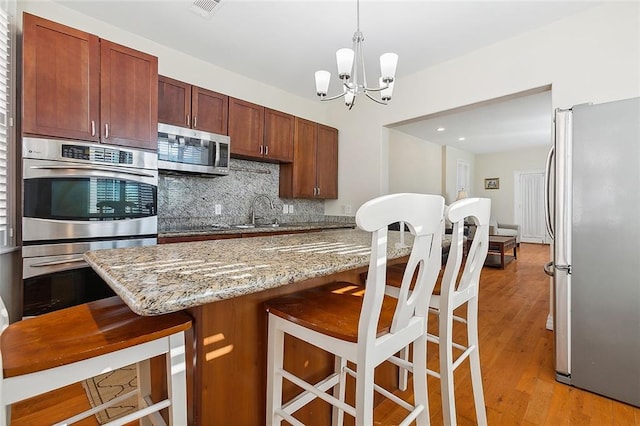 kitchen with appliances with stainless steel finishes, hanging light fixtures, light hardwood / wood-style floors, a kitchen bar, and a chandelier