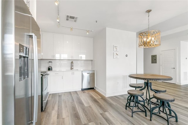 kitchen with hanging light fixtures, white cabinetry, appliances with stainless steel finishes, light hardwood / wood-style floors, and decorative backsplash