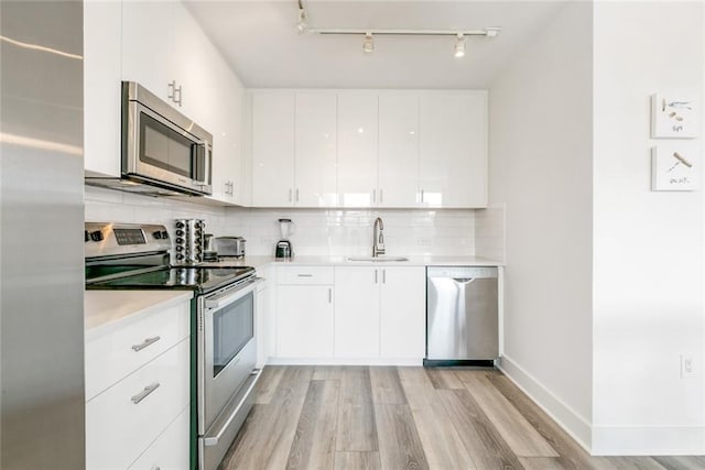 kitchen featuring sink, backsplash, white cabinetry, appliances with stainless steel finishes, and light wood-type flooring