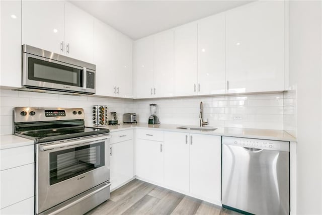 kitchen with appliances with stainless steel finishes, white cabinetry, sink, and light hardwood / wood-style flooring