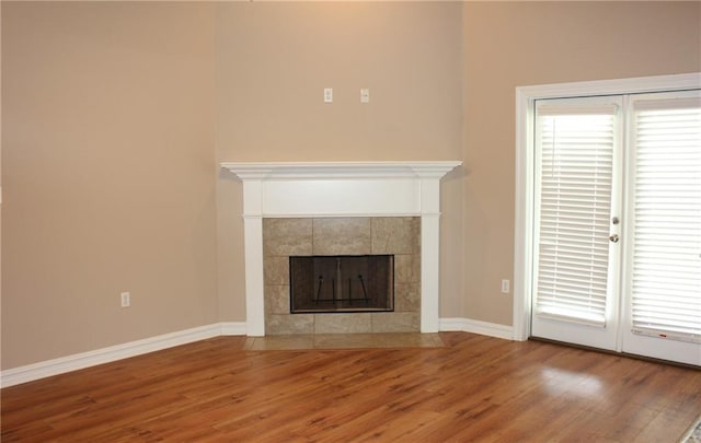 unfurnished living room featuring a tile fireplace, baseboards, and wood finished floors