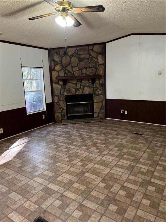 unfurnished living room featuring wood walls, a fireplace, ceiling fan, and a textured ceiling