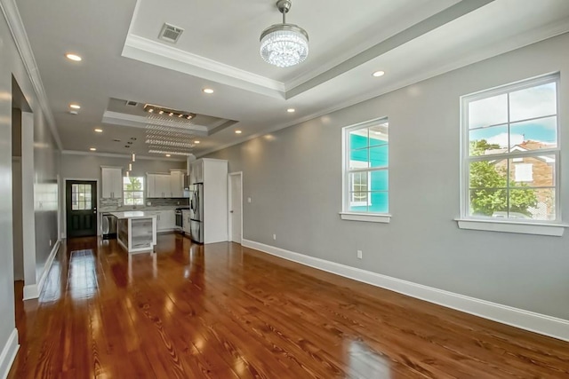 unfurnished living room featuring a raised ceiling, dark wood-type flooring, and a healthy amount of sunlight