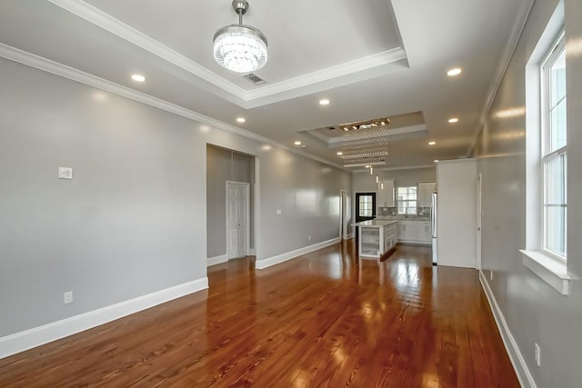 unfurnished living room featuring a raised ceiling, ornamental molding, dark hardwood / wood-style floors, and plenty of natural light