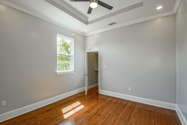 empty room featuring ornamental molding, wood-type flooring, ceiling fan, and a raised ceiling