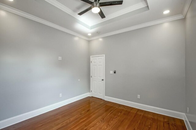 empty room with a raised ceiling, ornamental molding, hardwood / wood-style floors, and ceiling fan