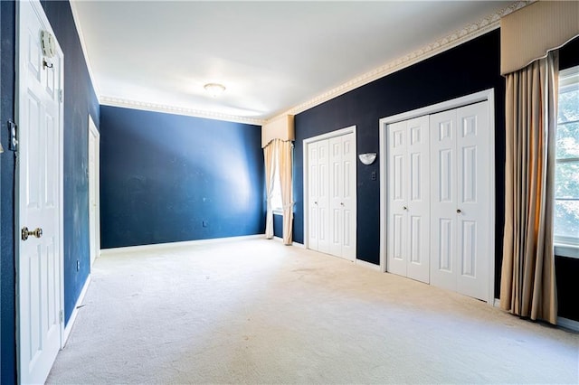 unfurnished bedroom with light carpet, ornamental molding, and two closets