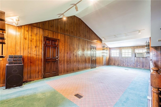 interior space with lofted ceiling, light colored carpet, wood walls, and rail lighting