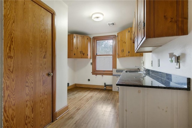 kitchen with light wood-type flooring, dark stone countertops, and sink