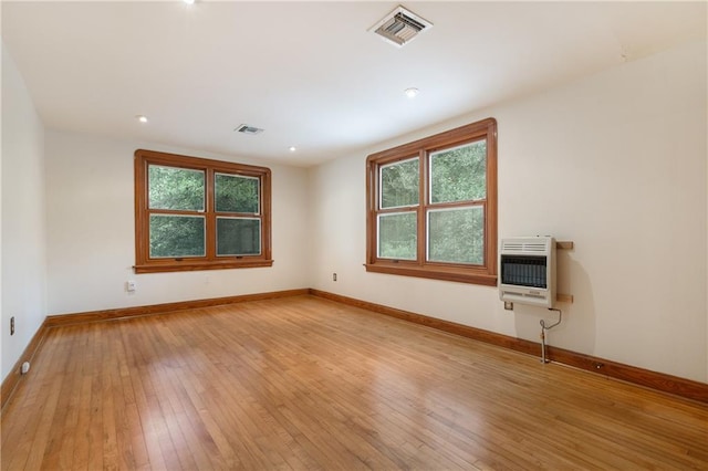 spare room featuring light hardwood / wood-style flooring, heating unit, and a wealth of natural light