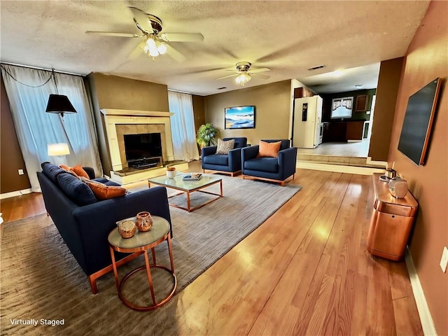 living room featuring a tile fireplace, a textured ceiling, hardwood / wood-style flooring, and ceiling fan