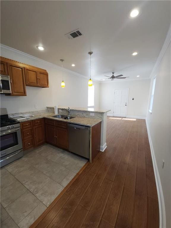 kitchen with light hardwood / wood-style floors, pendant lighting, sink, kitchen peninsula, and appliances with stainless steel finishes