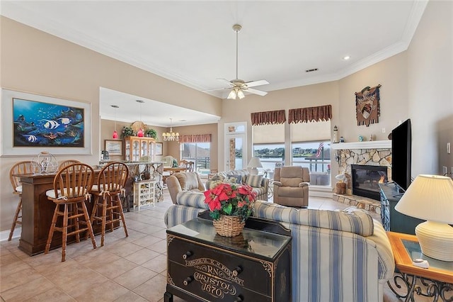 living room with ceiling fan with notable chandelier, a stone fireplace, crown molding, and light tile patterned flooring