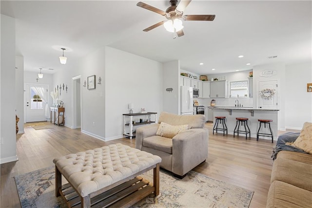 living room with light wood-type flooring, ceiling fan, and sink