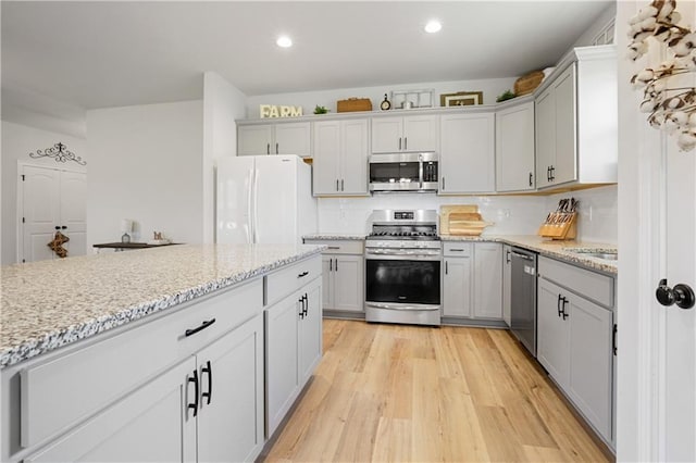 kitchen with light hardwood / wood-style flooring, decorative backsplash, appliances with stainless steel finishes, and light stone countertops