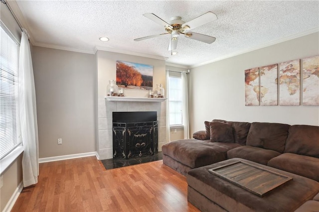 living room with a tile fireplace, a healthy amount of sunlight, crown molding, and hardwood / wood-style floors