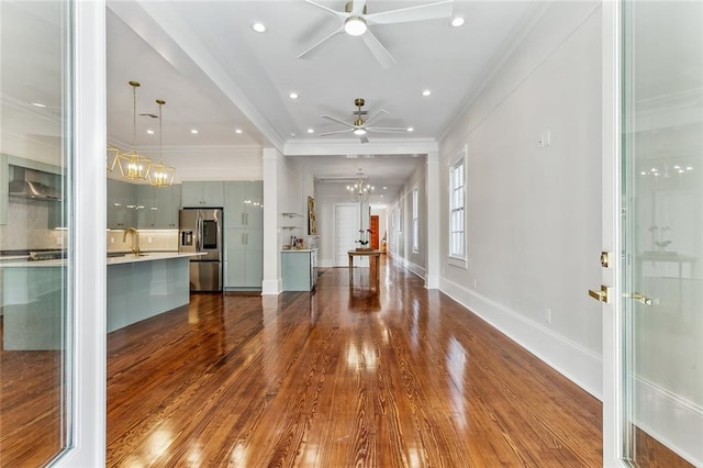 unfurnished living room with crown molding, ceiling fan with notable chandelier, hardwood / wood-style floors, and sink