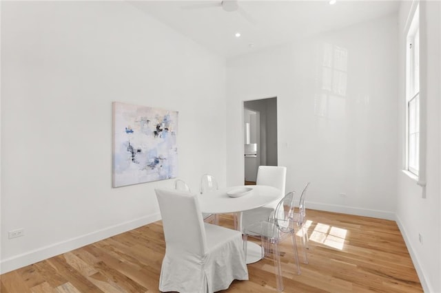 dining room with a towering ceiling, ceiling fan, and light hardwood / wood-style flooring