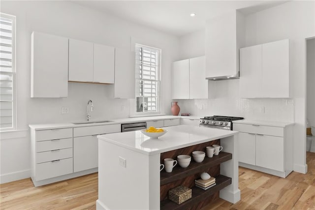 kitchen with light wood-type flooring, sink, white cabinetry, a kitchen island, and stainless steel appliances