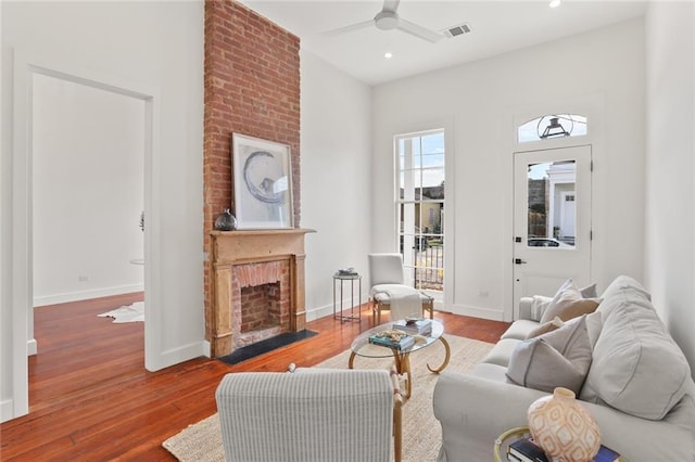 living room with a brick fireplace, ceiling fan, and hardwood / wood-style flooring