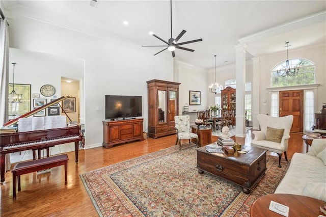 living room with hardwood / wood-style flooring, decorative columns, a high ceiling, ceiling fan with notable chandelier, and crown molding