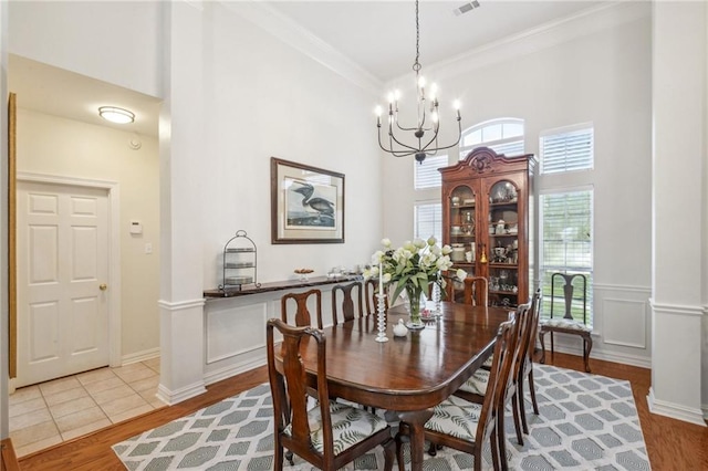 dining space featuring light hardwood / wood-style flooring, decorative columns, an inviting chandelier, and crown molding