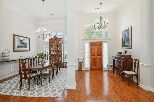 foyer entrance with ornamental molding, wood-type flooring, a notable chandelier, and decorative columns