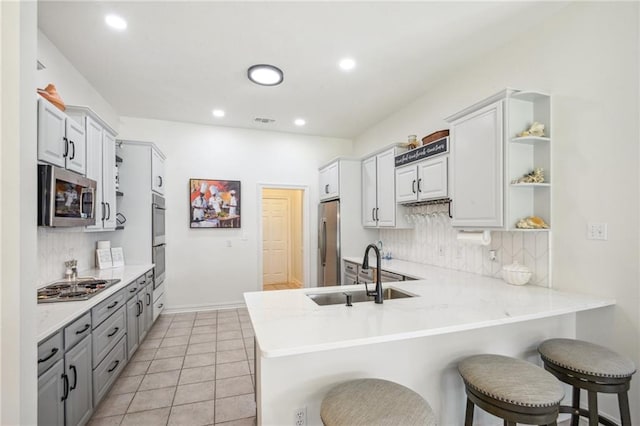 kitchen featuring light tile patterned floors, sink, kitchen peninsula, appliances with stainless steel finishes, and a kitchen bar