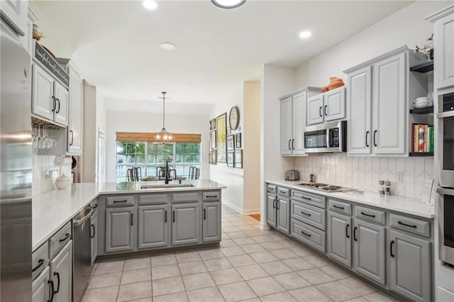 kitchen featuring gray cabinets, stainless steel appliances, kitchen peninsula, and pendant lighting