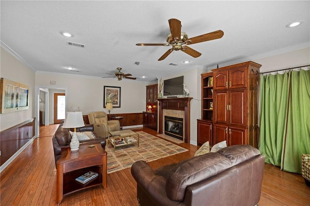 living room featuring ceiling fan, wooden walls, light hardwood / wood-style flooring, a tile fireplace, and crown molding