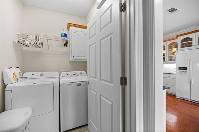 clothes washing area with cabinets, light hardwood / wood-style flooring, washer and dryer, and crown molding