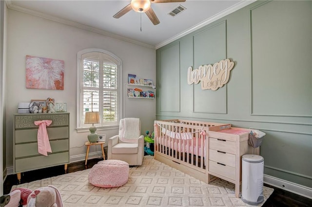 bedroom featuring a crib, light wood-type flooring, ornamental molding, and ceiling fan