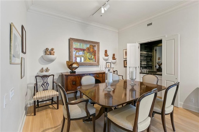 dining area featuring rail lighting, light hardwood / wood-style floors, and ornamental molding