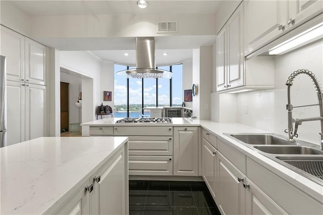 kitchen featuring island range hood, light stone countertops, stainless steel gas stovetop, and white cabinetry