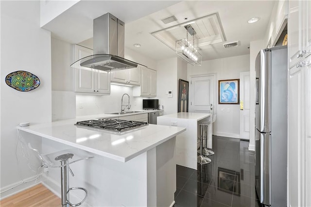 kitchen with white cabinets, kitchen peninsula, island range hood, stainless steel appliances, and a breakfast bar