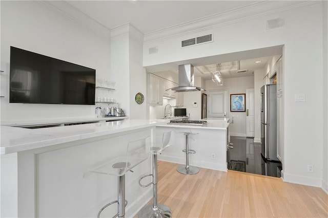 kitchen featuring white cabinets, kitchen peninsula, wall chimney range hood, a kitchen breakfast bar, and light wood-type flooring