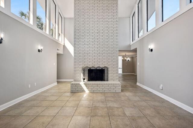 unfurnished living room with a high ceiling, a fireplace, an inviting chandelier, and light tile patterned floors