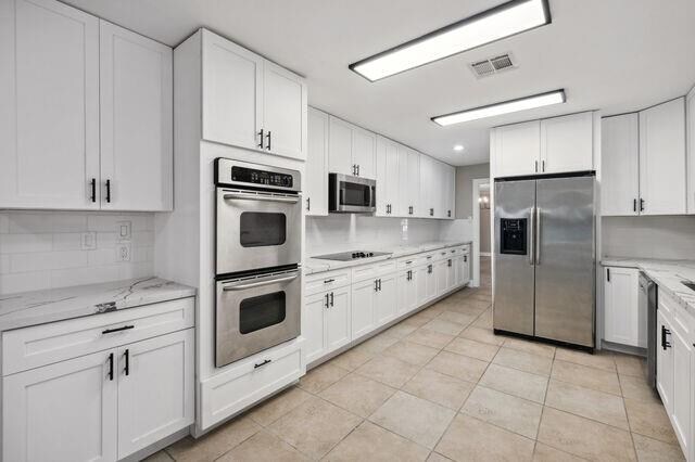 kitchen featuring appliances with stainless steel finishes, light tile patterned flooring, and white cabinets