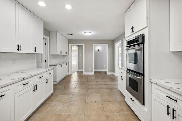 kitchen featuring stainless steel double oven, light stone countertops, plenty of natural light, and white cabinetry