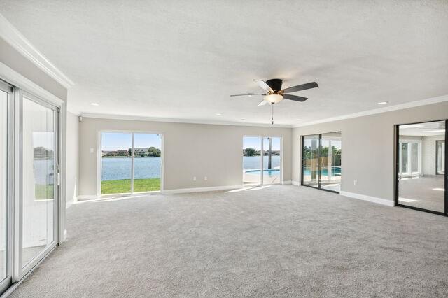 carpeted empty room featuring a water view, ceiling fan, and crown molding