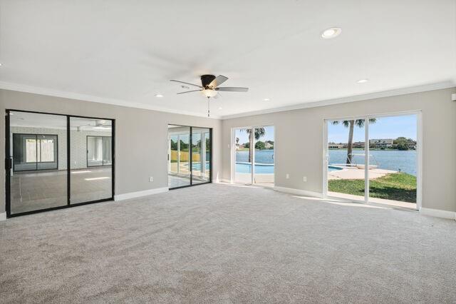 carpeted spare room featuring a water view, ceiling fan, a healthy amount of sunlight, and crown molding