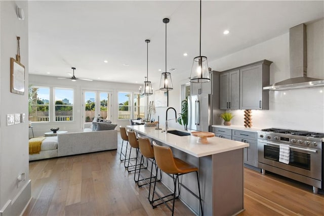 kitchen with appliances with stainless steel finishes, a kitchen breakfast bar, an island with sink, sink, and wall chimney range hood