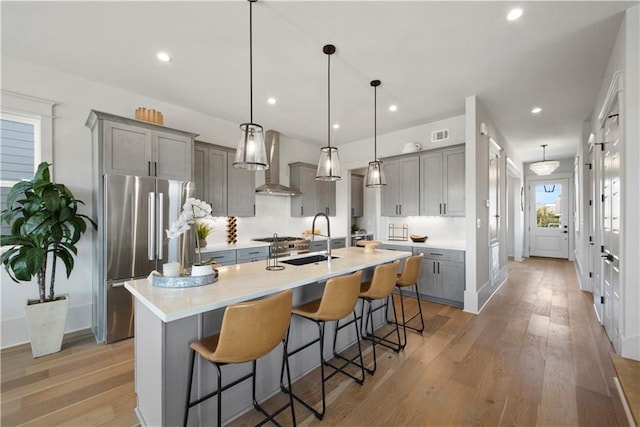 kitchen featuring appliances with stainless steel finishes, wall chimney exhaust hood, hanging light fixtures, and a breakfast bar