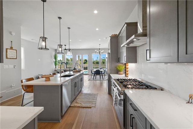 kitchen with light wood-type flooring, sink, hanging light fixtures, wall chimney exhaust hood, and stainless steel appliances