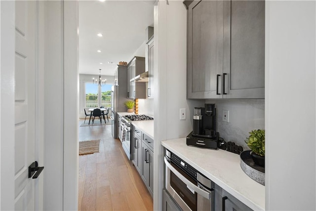 kitchen with gray cabinets, stainless steel appliances, a chandelier, and light hardwood / wood-style floors