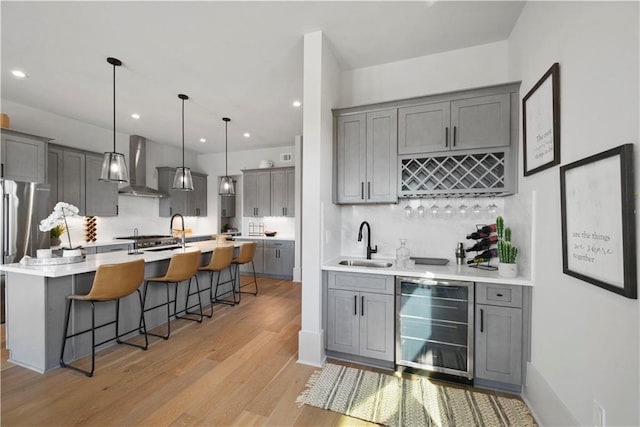 kitchen with beverage cooler, a center island with sink, wall chimney exhaust hood, decorative light fixtures, and a kitchen bar