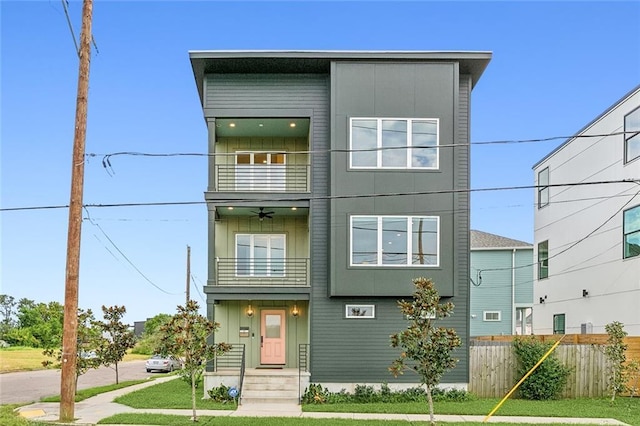 contemporary home with board and batten siding, a front yard, fence, and a balcony