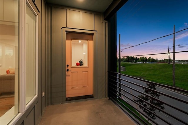 exterior entry at dusk featuring a lawn and a balcony